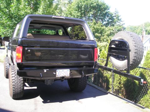 1995 Ford Bronco - The rear of a black Ford Bronco is shown with a custom bumper and a spare tire mounted on a swing-away carrier.