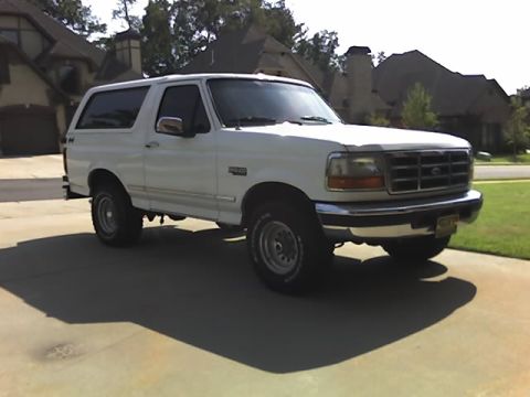1996 Ford Bronco - A white Ford Bronco is parked on a paved surface in front of a house.