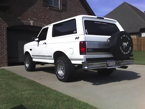 1996 Ford Bronco - 1996 Ford Bronco parked in front of a brick house, showing the rear and spare tire.