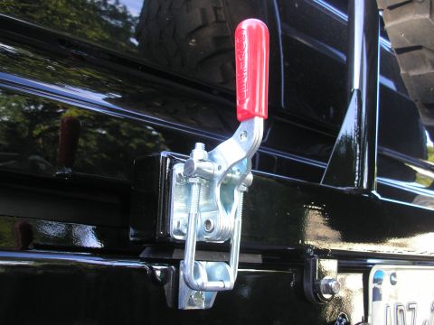 1995 Ford Bronco - Close-up of a red-handled toggle clamp attached to the rear bumper of a black vehicle, with a spare tire visible.
