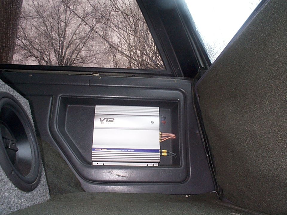 Car amplifier labeled V12 and subwoofer installed in vehicle interior