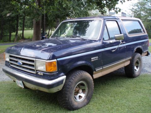 1989 Ford Bronco - This Ford Bronco features a two-tone paint scheme and a roof rack, parked outdoors on a grassy lawn.