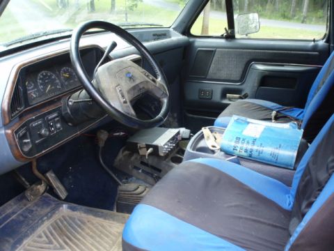 1989 Ford Bronco - The interior of a truck shows the dashboard, steering wheel, and a shop manual on the passenger seat.