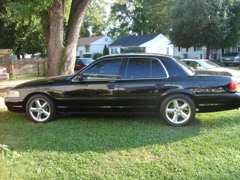 1993 Ford Crown Victoria - Driver-side profile view of a black full-size four-door sedan parked on grass, fitted with aftermarket chrome/machined five-spoke wheels an…