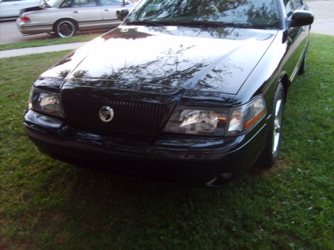 1993 Ford Crown Victoria - Front three-quarter close-up of a glossy black Mercury Marauder-style sedan parked on grass, showing its blacked-out grille with Mercury em…
