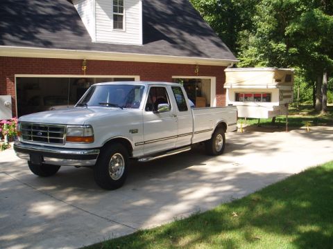 1980 Ford Bronco - A white Ford F-250 pickup truck is parked in a driveway next to a house, with a camper unit in the truck bed.