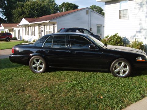 1993 Ford Crown Victoria - Driver-side profile of a black full-size sedan parked on a residential lawn, wearing chrome five-spoke wheels and dark-tinted windows with…