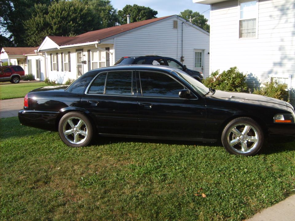 Black full-size sedan in profile on a lawn with chrome five-spoke wheels