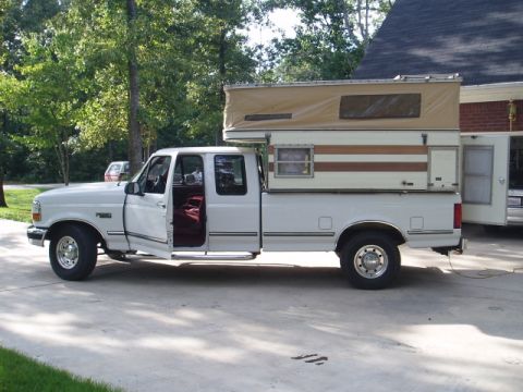 1980 Ford Bronco - A white Ford F-250 pickup truck with a camper shell is parked on a concrete driveway. The driver's side door is open, revealing red interio…