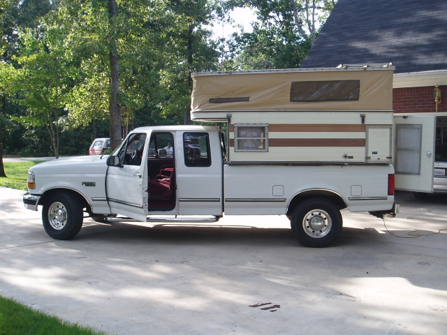 White Ford F-250 pickup truck with camper shell and open driver's door.