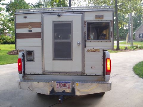 1980 Ford Bronco - The rear of a white truck camper is shown, mounted in the bed of a pickup truck. The camper has a door, two windows, and a chrome bumper wi…
