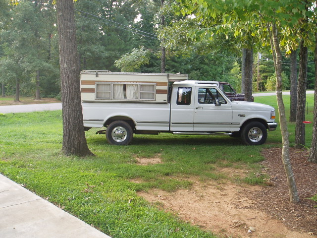 White Ford F-Series pickup truck with camper shell parked on grass.