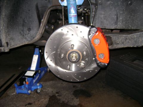1991 Ford Taurus - Close-up of a vehicle's front brake assembly, an orange caliper and a drilled rotor, with a blue jack visible.