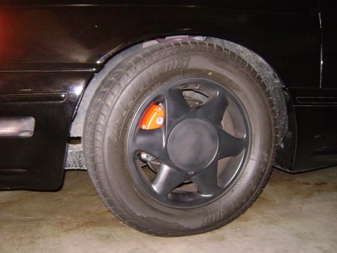 1991 Ford Taurus - Close-up of a car's wheel and brake assembly, showing the tire and black five-spoke rim.