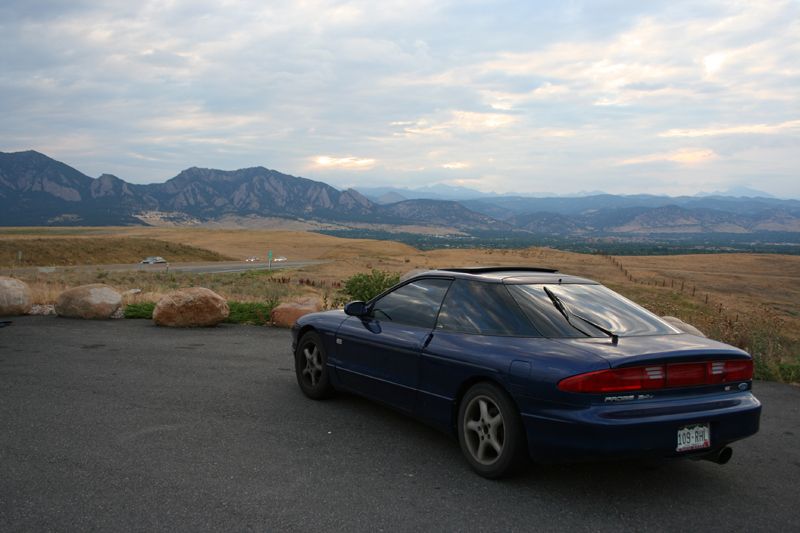 Blue 1995 Ford Probe coupe parked on asphalt, rear 3/4 view, with mountains and a cloudy sky