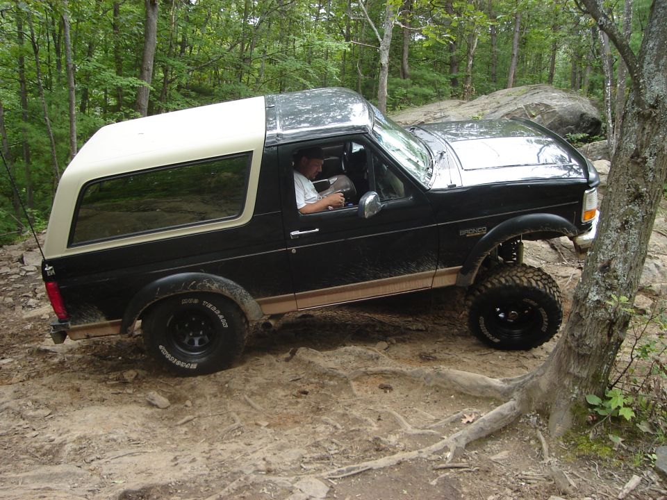 Black 1995 Ford Bronco with a white top driving on a rocky trail