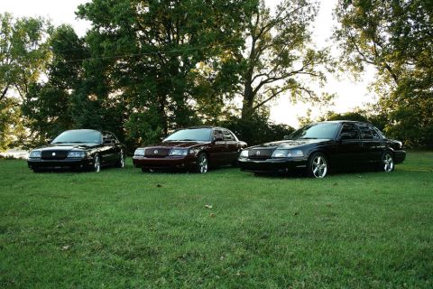 2003 Mercury Marauder - Three Mercury Marauders are lined up on a grassy lawn with trees behind them.