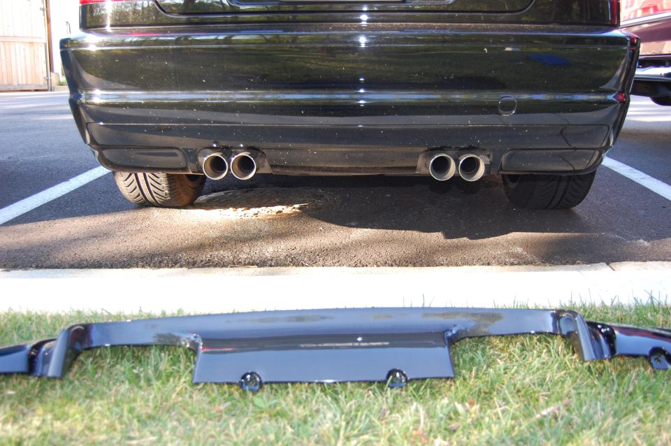 2002 BMW M3 rear bumper with quad exhaust tips, and a separate CSL diffuser laid on grass