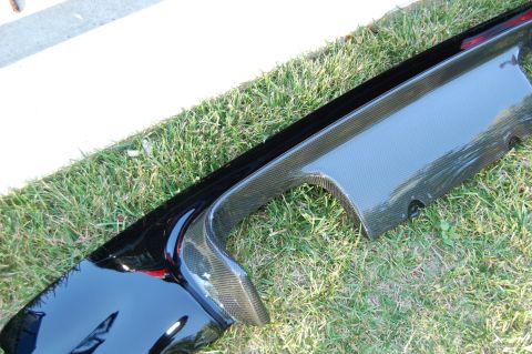 2002 BMW M3 - A close-up of a carbon fiber rear diffuser part resting on a grassy surface.