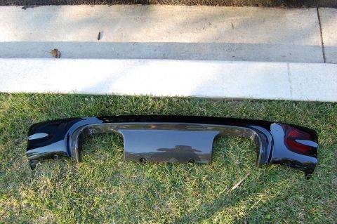 2002 BMW M3 - A black aftermarket rear bumper diffuser lies on grass, showing its unique design and cutouts for exhaust and license plate.