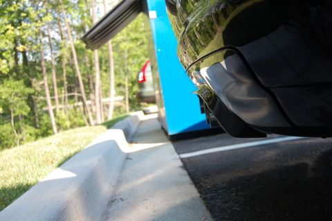 2002 BMW M3 - A black vehicle's rear bumper and exhaust are shown, with another car parked nearby.
