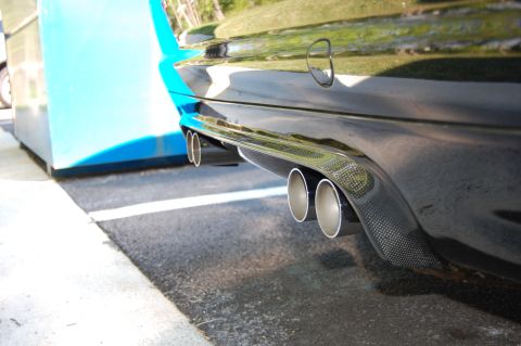 2002 BMW M3 - Close-up of a car's rear bumper and quad exhaust pipes, with a carbon fiber diffuser visible.