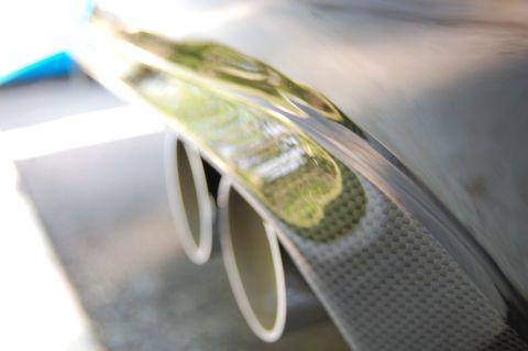 2002 BMW M3 - Close-up of a carbon fiber rear bumper dual exhaust pipes, with a reflection of greenery.