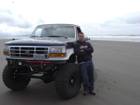 1993 Ford Bronco - Person standing next to a lifted Ford Bronco on a sandy beach with the ocean in the background.