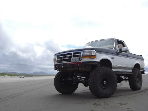 1993 Ford Bronco - This modified Ford Bronco is parked on a sandy beach under a cloudy sky.