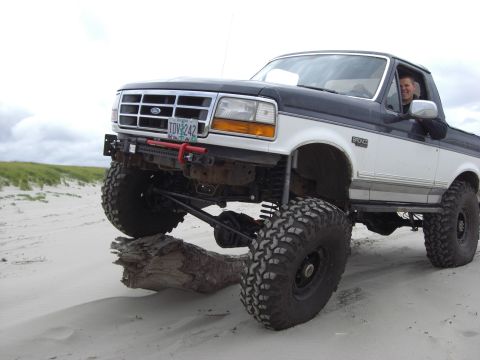 1993 Ford Bronco - This lifted 1992 Ford Bronco is shown off-road on a sandy terrain, prominent large tires and a two-tone paint scheme.