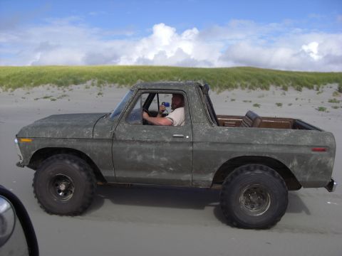 1993 Ford Bronco - Ford Bronco with custom paint driving on a beach under a cloudy sky.