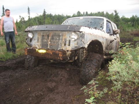 1990 Ford F-250 - A man watches as a heavily mud-caked truck becomes stuck in a muddy off-road area.