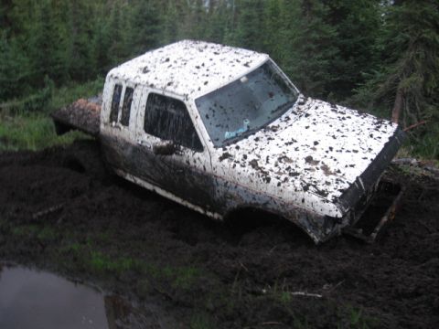 1990 Ford F-250 - This 1990 Ford F-250 is deeply stuck in thick mud, with its white body covered in dirt.