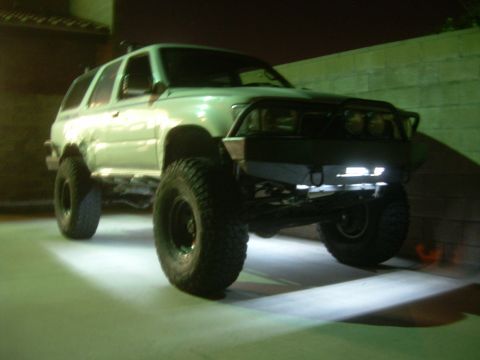 1993 Toyota 4Runner - Modified white SUV with off-road tires and custom bumper illuminated by rock lights.