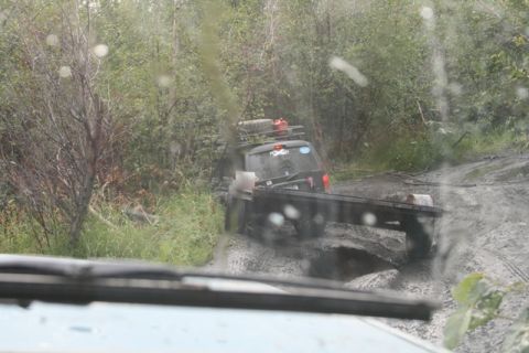 1990 Chevrolet Suburban - A black SUV navigates a muddy trail, its rear end partially submerged in thick mud.