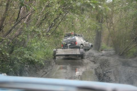 1990 Chevrolet Suburban - A black SUV navigates a muddy path, towing a trailer through a wooded area.