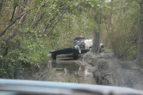 1990 Chevrolet Suburban - An off-road vehicle navigates a challenging muddy path while towing a trailer.