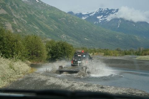 1990 Chevrolet Suburban - SUV and trailer navigating a water crossing with a scenic mountain backdrop.
