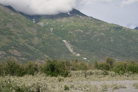 1990 Chevrolet Suburban - A vast mountain landscape unfolds under a cloudy sky, with lush green vegetation covering the slopes and low brush in the foreground.