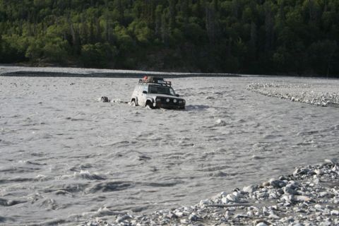 1990 Chevrolet Suburban - A silver SUV with a trailer is being towed through a rocky riverbed.