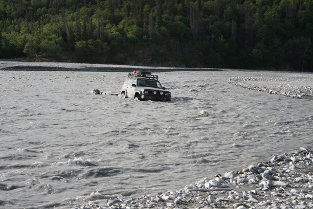Silver SUV being towed through a shallow river, trailer attached
