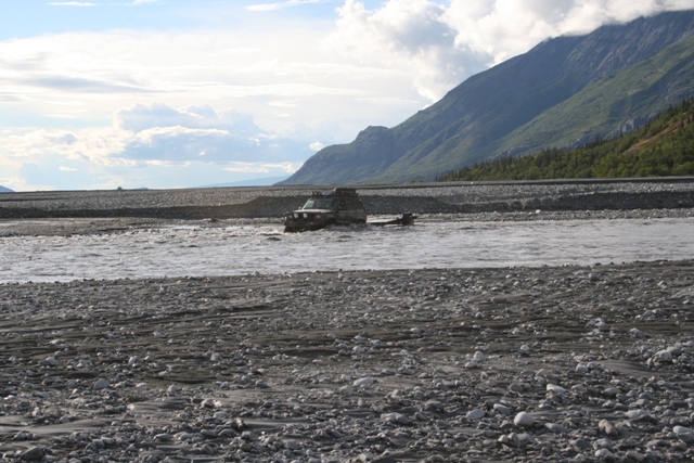 Off-road vehicle partially submerged in a rocky riverbed with mountains in background