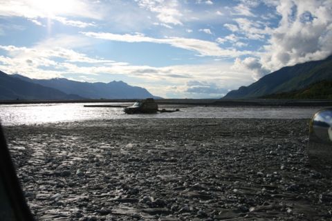 1990 Chevrolet Suburban - An SUV is stuck in a riverbed under a cloudy sky with mountains in the distance.