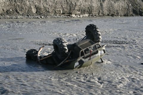 1990 Chevrolet Suburban - An ATV is overturned in a shallow, muddy river, with its wheels in the air.