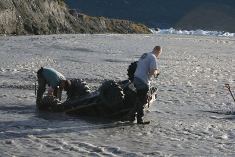 1990 Chevrolet Suburban - Two individuals work to recover an overturned ATV from a rocky, shallow riverbed.