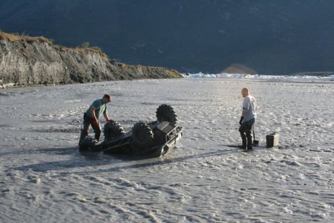 1990 Chevrolet Suburban - Two individuals attempt to recover an overturned ATV from a shallow, muddy riverbed.