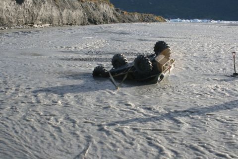 1990 Chevrolet Suburban - An ATV is overturned in a muddy river, partially submerged and attached to a tow strap, with a shovel nearby.