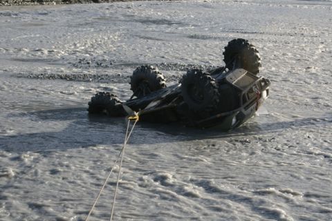 1990 Chevrolet Suburban - An ATV is overturned in a shallow, muddy river, with a tow rope attached.
