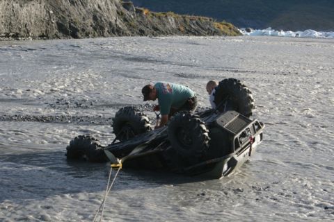 1990 Chevrolet Suburban - Two individuals work to recover an ATV that has overturned in a shallow, rocky riverbed.