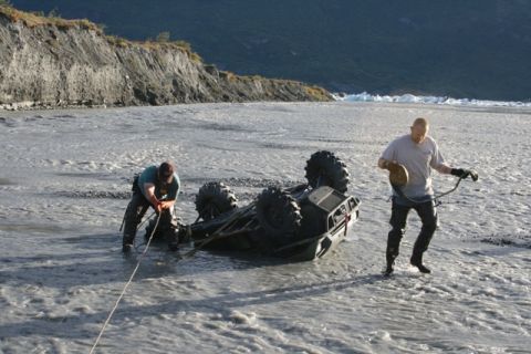 1990 Chevrolet Suburban - Two individuals work to recover an overturned ATV from a shallow, rocky riverbed.